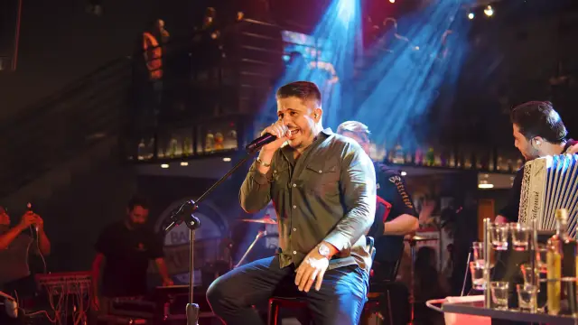 Eder de Oliveira cantando sentado no palco, com sanfoneiro ao lado